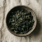 Ciotola rustica con foglie di tè oolong, su sfondo di lino neutro.