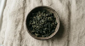 Ciotola rustica con foglie di tè oolong, su sfondo di lino neutro.